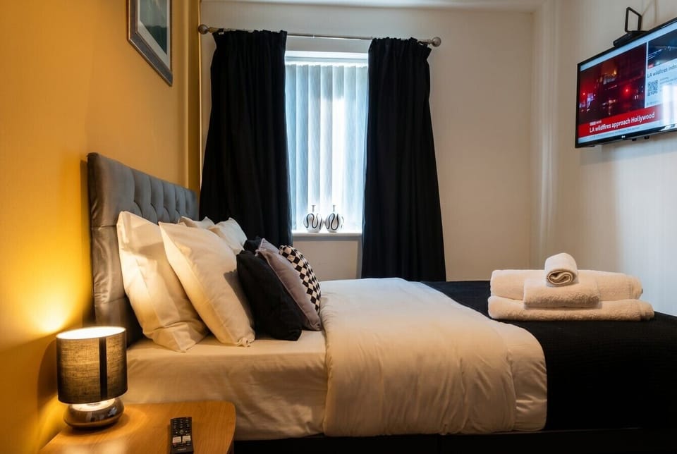 Another angle of the yellow double bedroom, with a wall-mounted smart TV above the bedside.