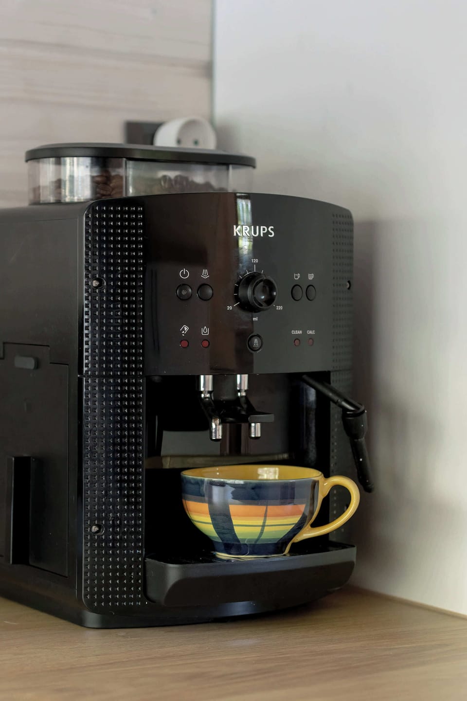 A black espresso machine is captured in detail, ready to serve coffee in a modern kitchen setting.
