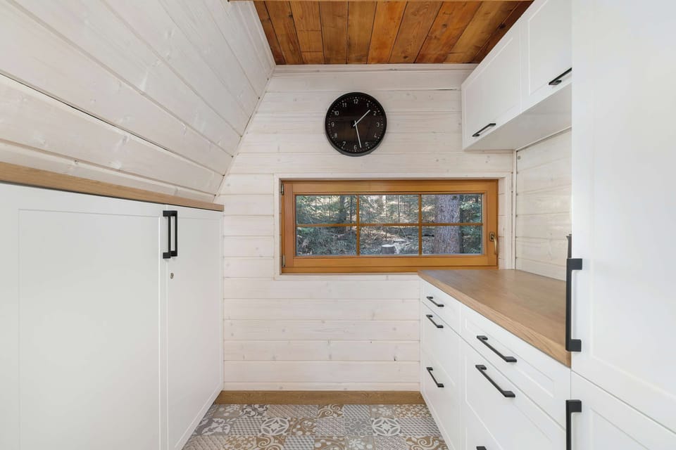 A minimalist hallway area features white storage cabinets and a horizontal window showing the greenery outside.