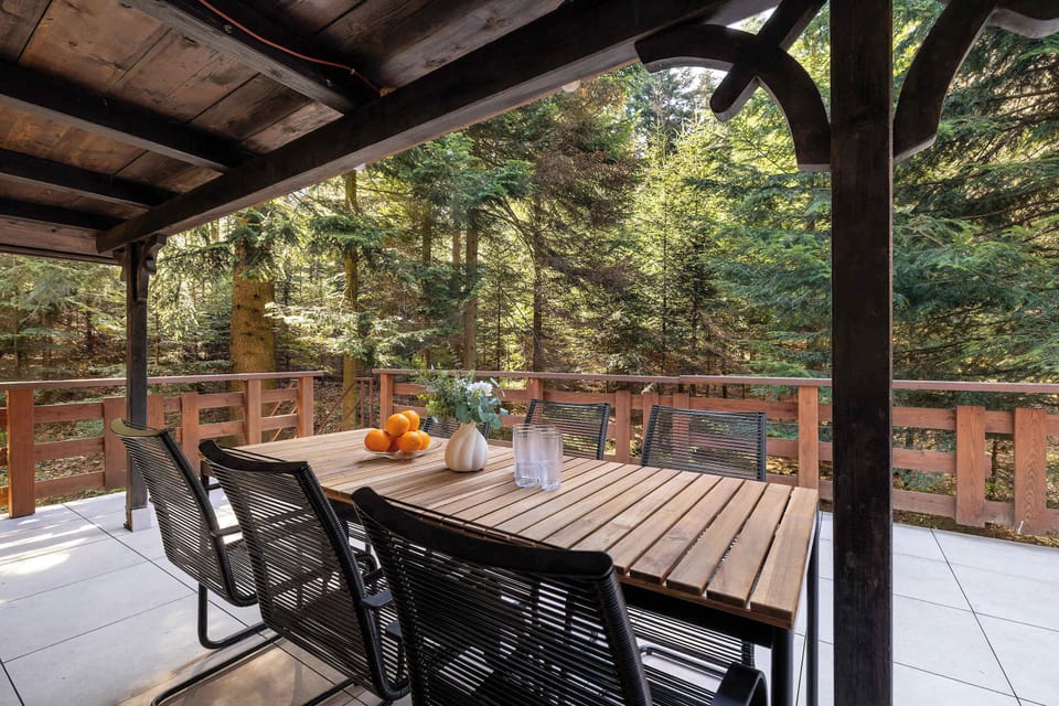An elevated wooden terrace provides a peaceful outdoor dining spot with a black metal table set and views of the dense surrounding forest.