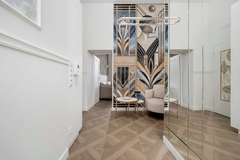 The hallway features white walls with decorative molding and consistent herringbone wood flooring. A mirrored wall section at the end reflects a decorative mural, making the corridor feel much larger.