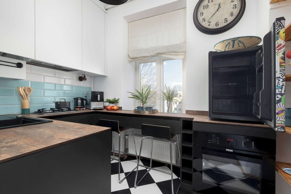 A view of the kitchen showing a modern range hood, a cooktop, and a black built-in oven under the countertop. The black appliances contrast with the white wall cabinets and the light-colored tiles on the wall.