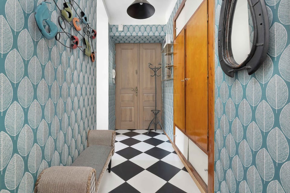 A stylish entryway with a wardrobe featuring mirrored doors that visually expand the narrow passageway. The wall covered in blue wallpaper with a geometric pattern creates an interesting visual effect with the checkerboard floor.