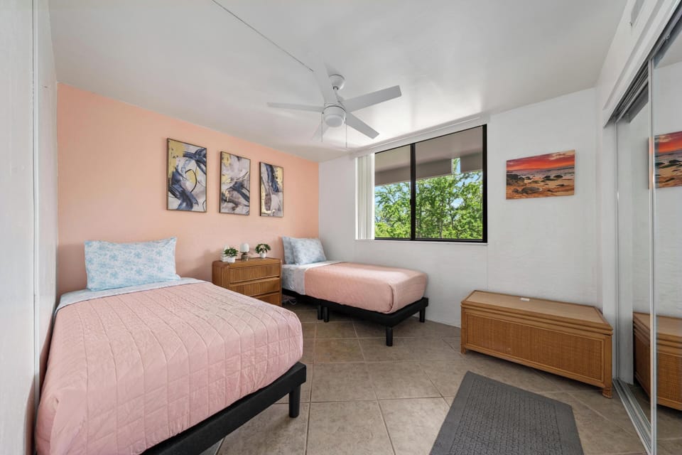 Rest peacefully in your bright twin bedroom with stylish coral accents, natural garden views, and cooling ceiling fan overhead.