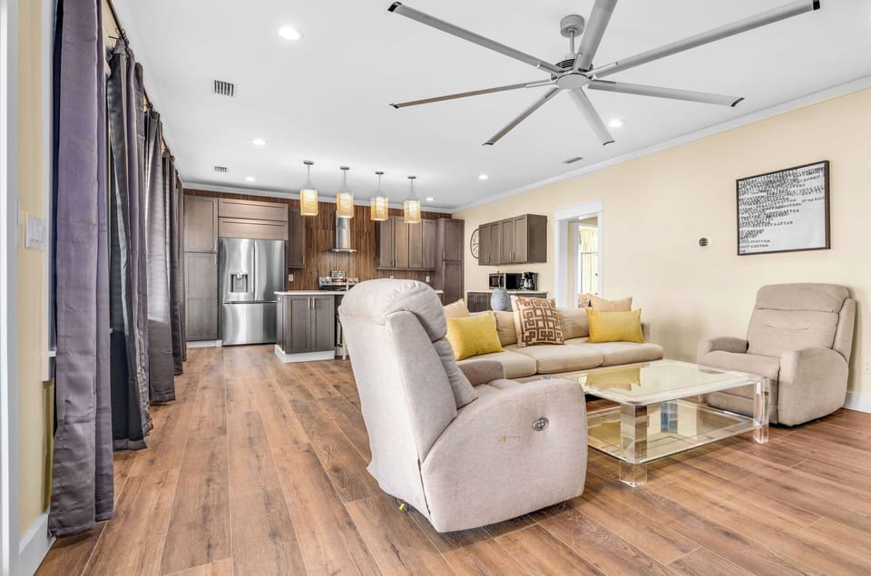 Relax in your spacious open-concept living area with plush recliners, modern kitchen, and soaring ceilings with stylish fan.