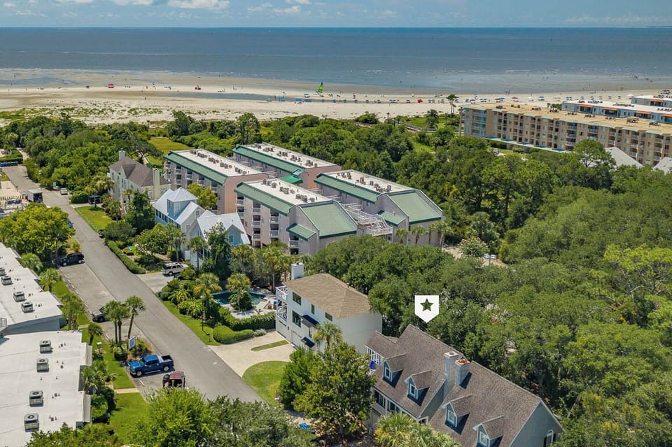 Aerial view showcasing the property's prime beachfront location, nestled among lush trees just steps from the pristine sandy shore.