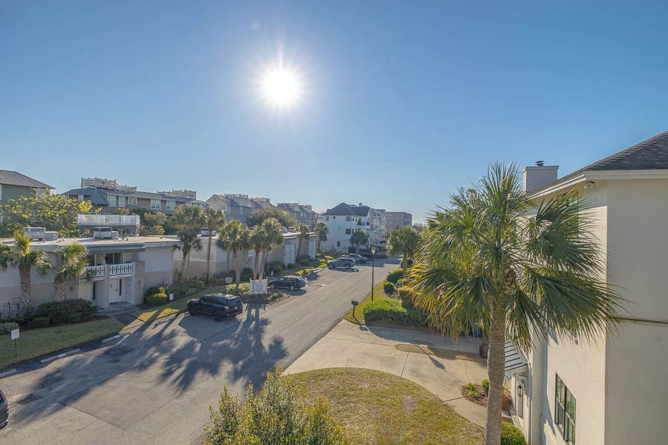 Bright sun illuminates this coastal residential community with palm trees and well-maintained grounds stretching toward nearby buildings.