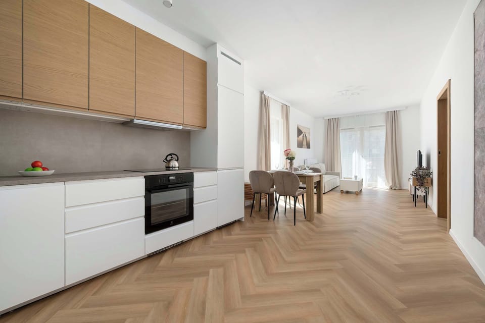 A living room with a comfortable sofa, a TV on a low stand, and a wooden floor arranged in a herringbone pattern. The space feels warm and inviting, ideal for relaxing after a long day.