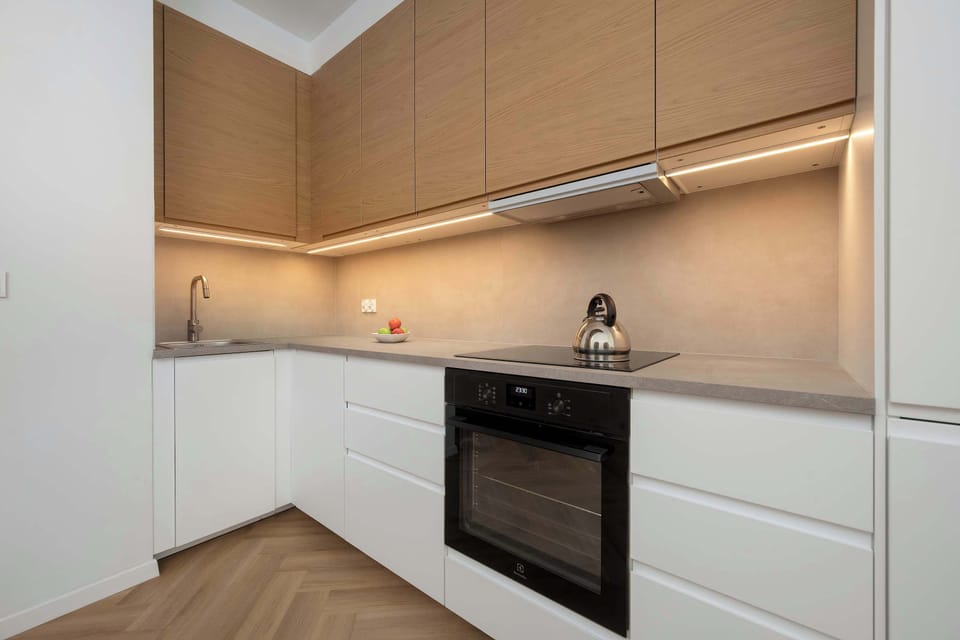 A compact, modern kitchenette with white cabinetry and a built-in oven, complemented by warm wooden accents. Clean lines and minimal design give the space a sleek and functional character.