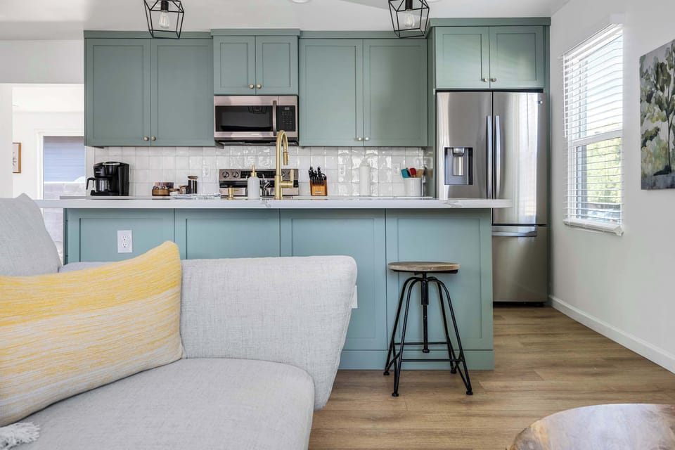 Step inside to a beautifully designed open-concept living space featuring sage green cabinetry, a fully equipped kitchen, and cozy living area.