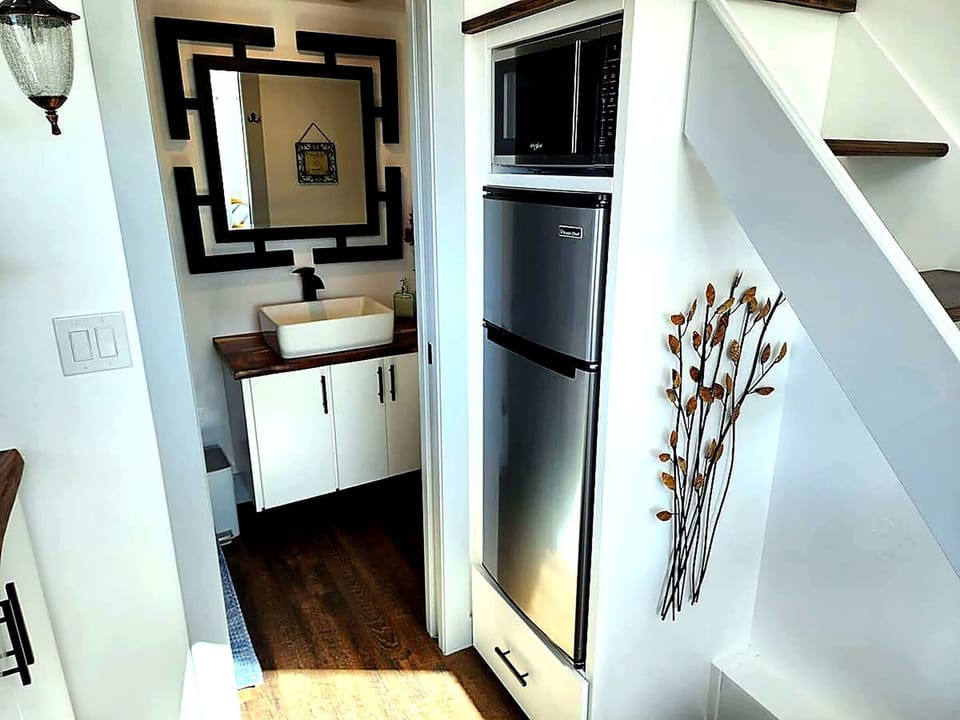 Compact yet functional kitchen with two-burner cooktop, refrigerator and freezer, microwave, and cabinet storage, ideal for quick breakfasts or relaxed dinners in your tiny home retreat.
