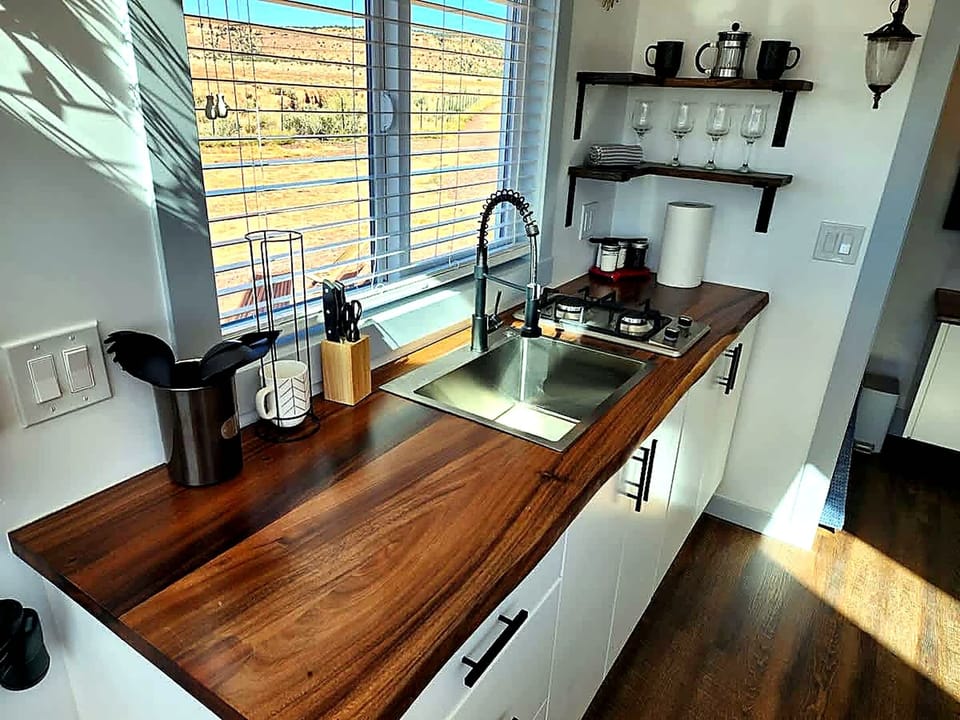Bright tiny home kitchen with butcher block counters, stainless sink, and two-burner cooktop. Includes microwave, coffee maker, and open shelving, perfect for easy meals before exploring Zion.