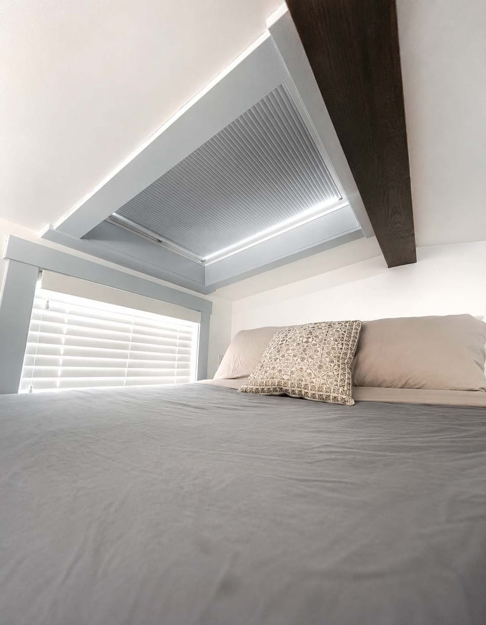 Queen bed loft with low ceilings, skylight, and window blinds for added privacy. Warm, inviting space with plush bedding, perfect for a peaceful night’s sleep in this thoughtfully designed tiny home.