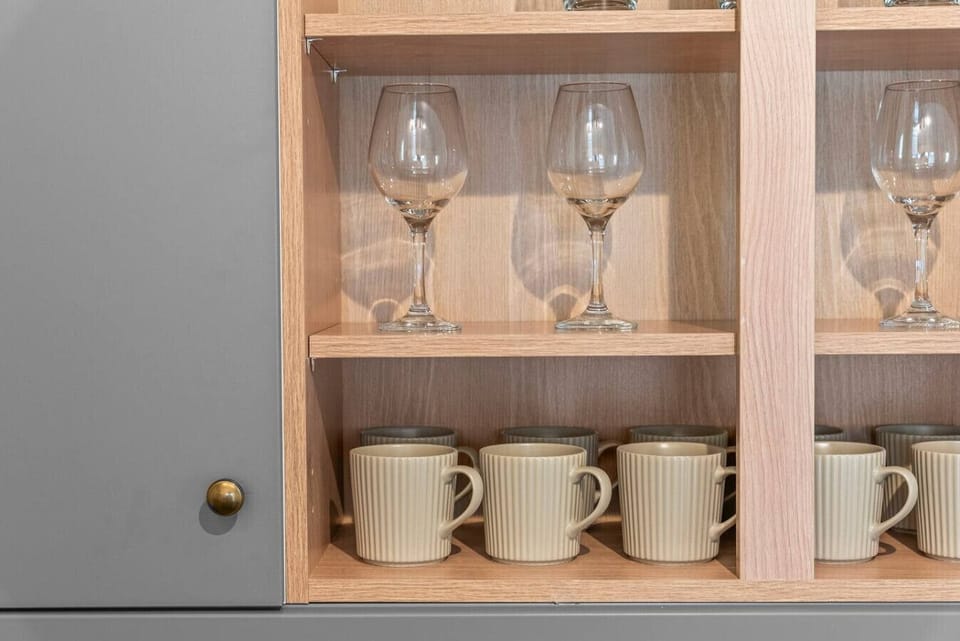 Kitchen shelving with glasses, mugs, and cups available for guest use.