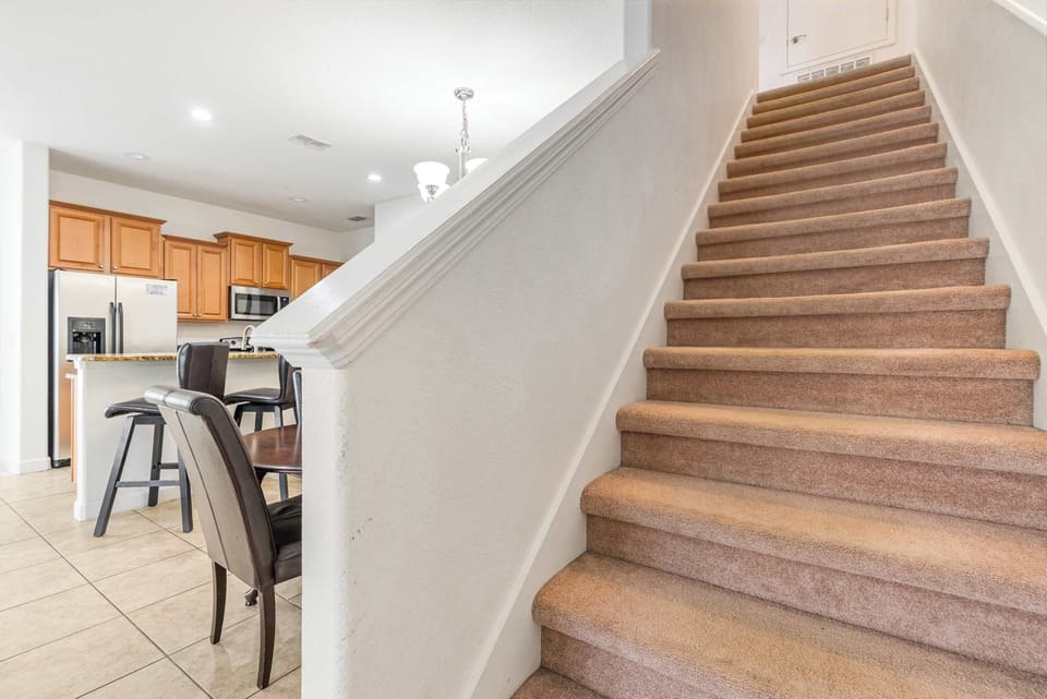 Carpeted stairs lead up from the open kitchen and dining area with wooden cabinetry and stainless steel appliances.