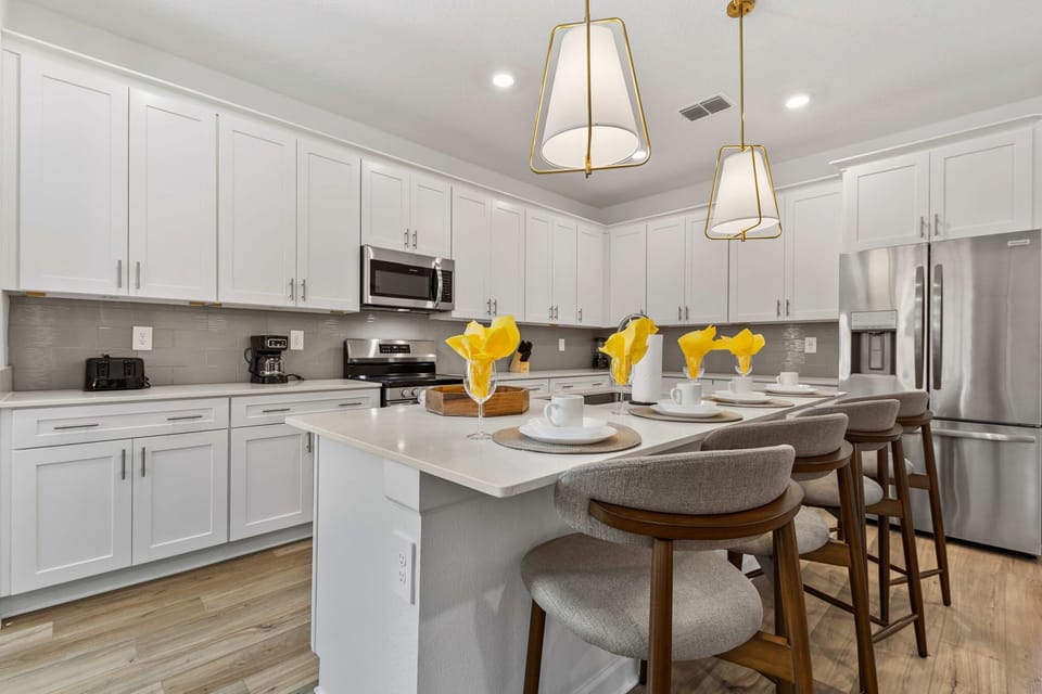 Sparkling chef's kitchen with white shaker cabinets, quartz island seating for 5, brass pendants, and stainless appliances-perfect for family breakfasts and meal prep!