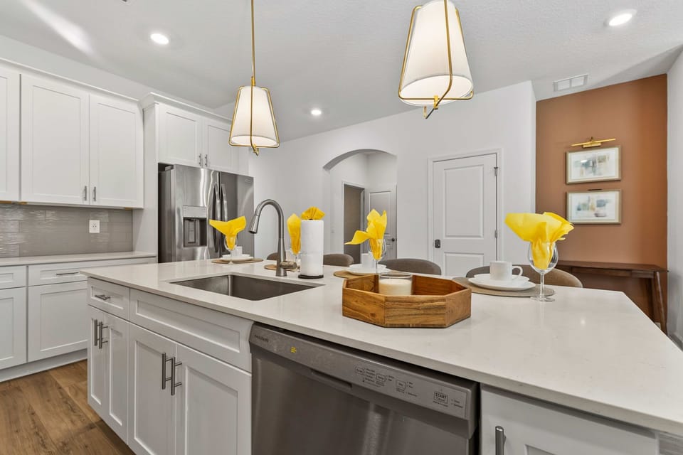 Central island with deep sink, sleek quartz, and gold-accent pendants-gather for snacks while the chef cooks in this open, modern space.