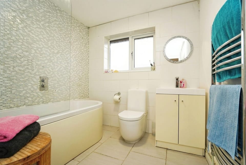 Family bathroom with mosaic tile surround, bathtub, and heated towel rail.