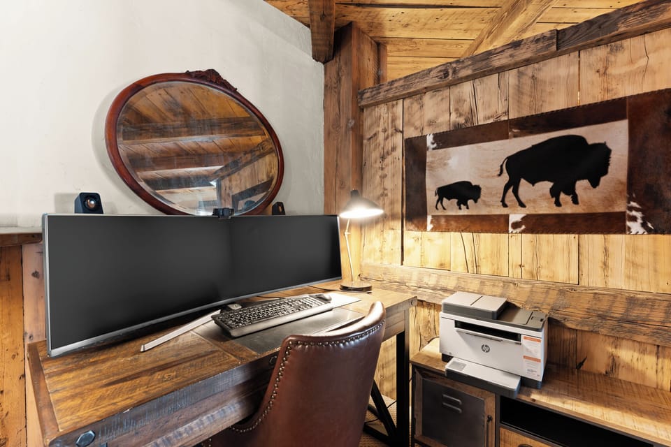 Your personal workspace blends rustic charm with modern convenience, featuring a spacious wooden desk, ergonomic seating, and ambient lighting beneath reclaimed timber beams that create a warm, inspiring atmosphere for productivity.