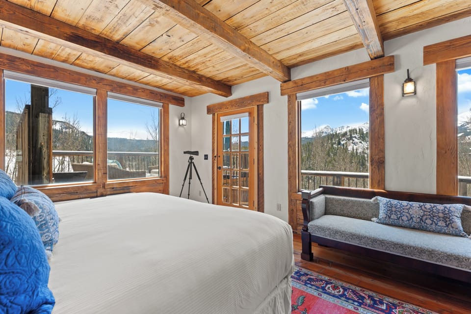 Wake up to breathtaking mountain views from this stunning bedroom with rustic wood beams and a cozy private balcony—your perfect alpine retreat awaits.