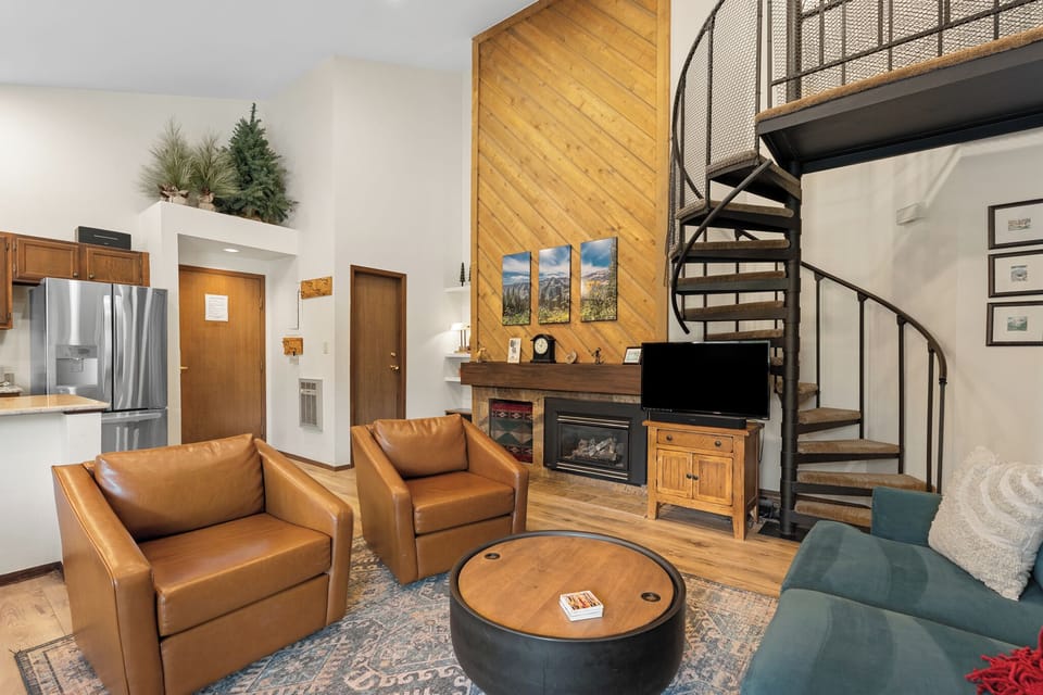 Settle into plush leather seating in your private living room, where a cozy fireplace awaits beneath soaring wood-paneled ceilings and a dramatic spiral staircase to your loft above.