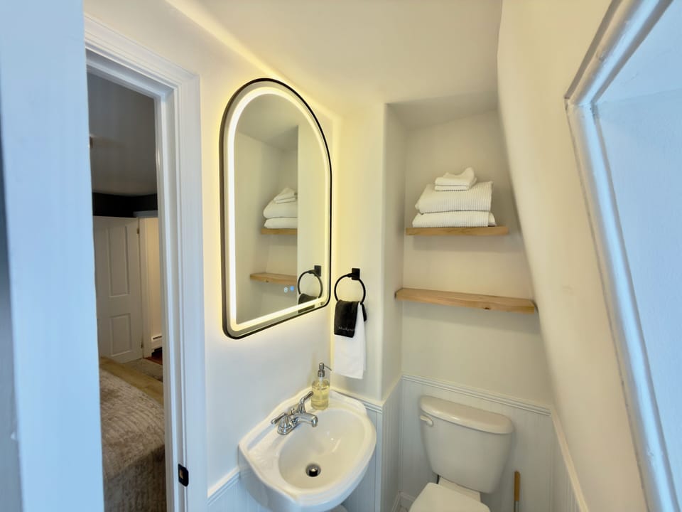 Bright powder room with backlit mirror, towels, and essentials