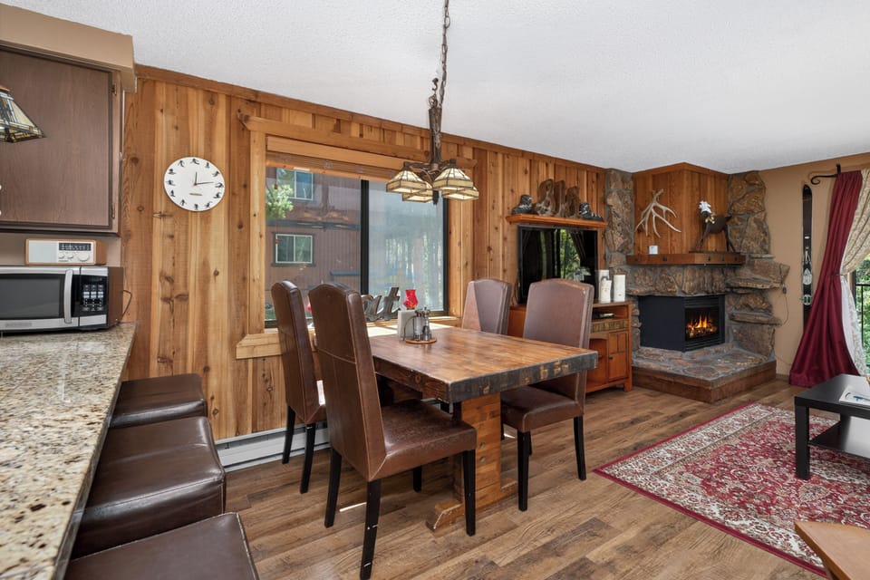 Gather around your rustic dining table beside the crackling stone fireplace, where warm wood tones and mountain charm create perfect moments for meals and memories.