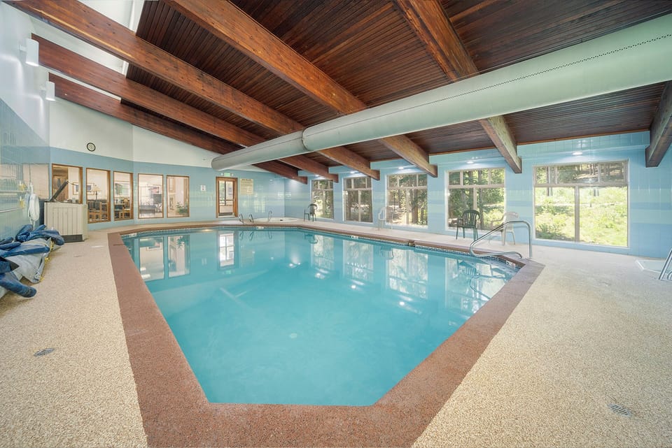 Dive into your private indoor pool sanctuary with stunning exposed wood beams overhead and forest views surrounding you.