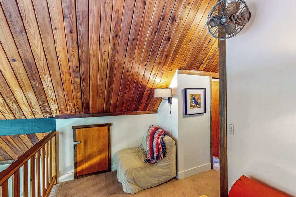Your loft lounge tucks under warm redwood planks — grab a blanket, sink into the armchair, and let the creek serenade you.