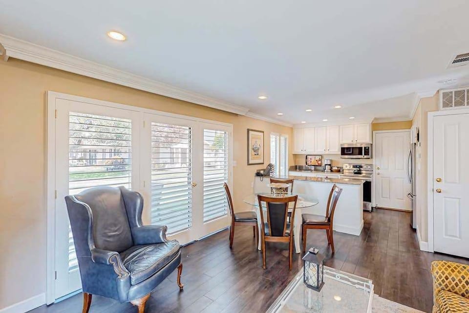 Gather around the glass-top dining table in your bright, open-concept living space with elegant plantation shutters and effortless flow to the kitchen