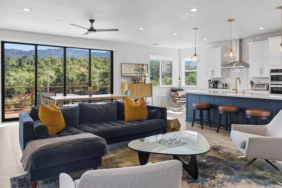 Gather around the glass coffee table with friends — kitchen, dining, and that ridge-line view all within easy conversation.