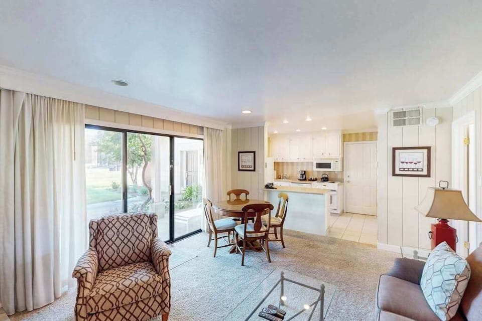 Settle into your open-concept living space with golf course views streaming through floor-to-ceiling sliders — kitchen, dining, and lounge all in one bright room.