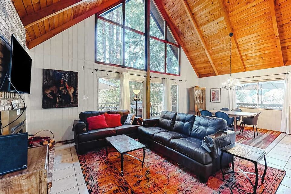 Soaring A-frame ceilings clad in warm wood frame your living room — sink into leather sofas and gaze through floor-to-ceiling redwood canopy windows.