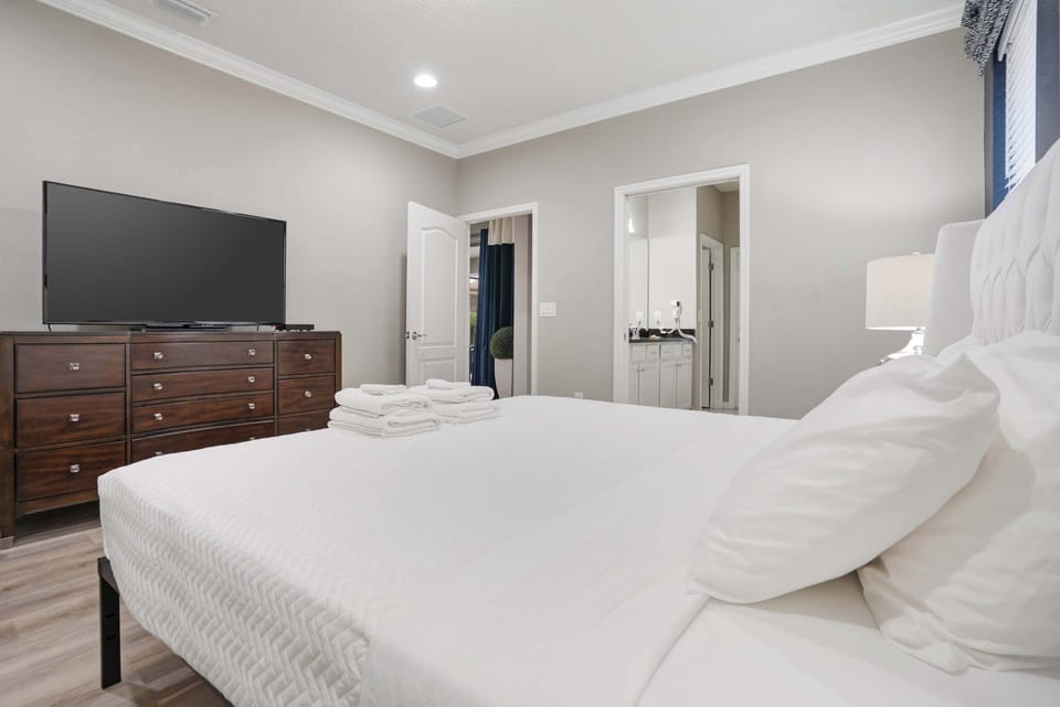 Modern bedroom with a large flat-screen TV and soft white bedding for a restful stay.