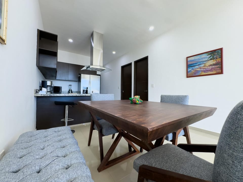 Dining area with dark wood table, gray upholstered chairs, tufted bench, and beach painting on white wall.