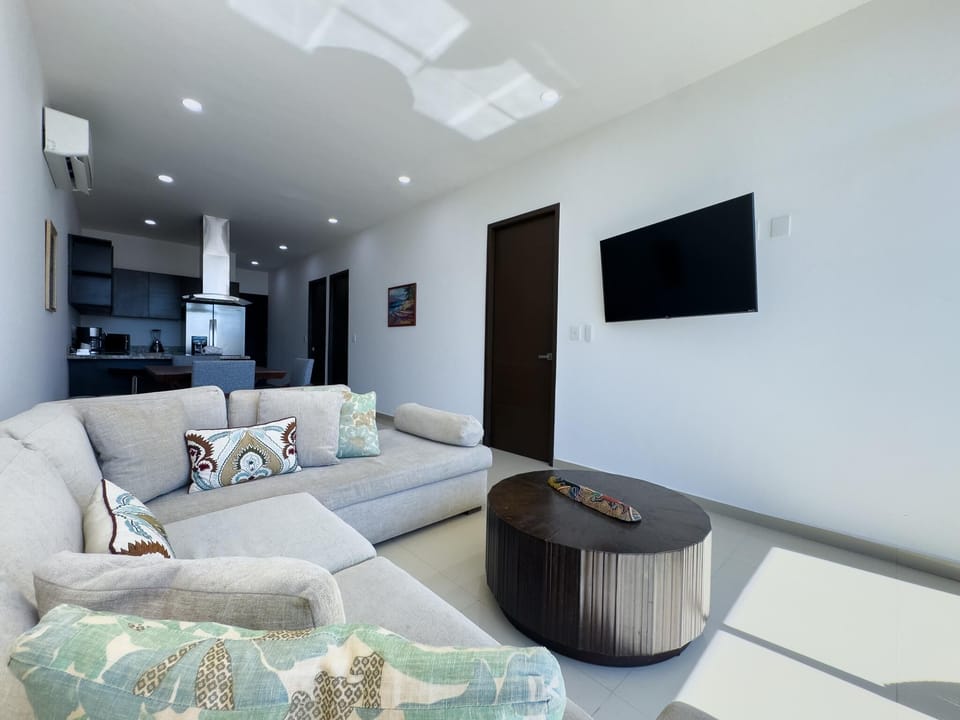 Light gray sectional sofa faces wall-mounted TV above a round dark wood coffee table in the living area.