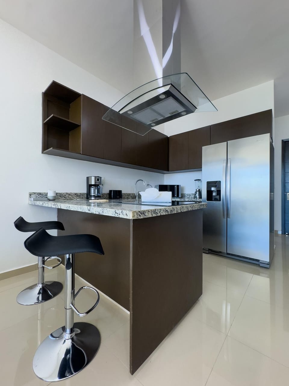 Two black bar stools sit at a granite-topped kitchen island beneath a curved glass range hood.