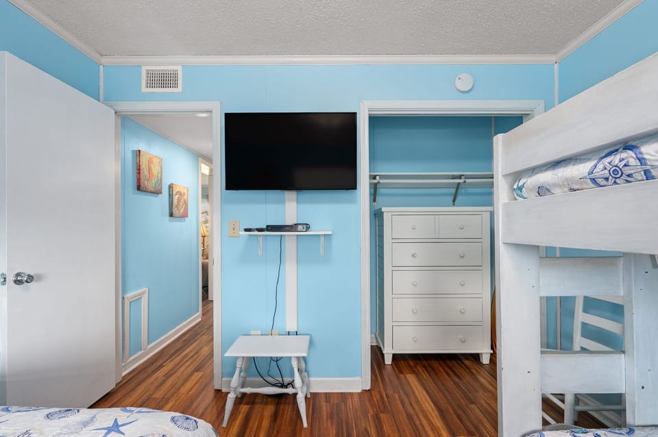 Bedroom with queen and twin bunk bed, attached full bathroom, light blue walls, and smart tv