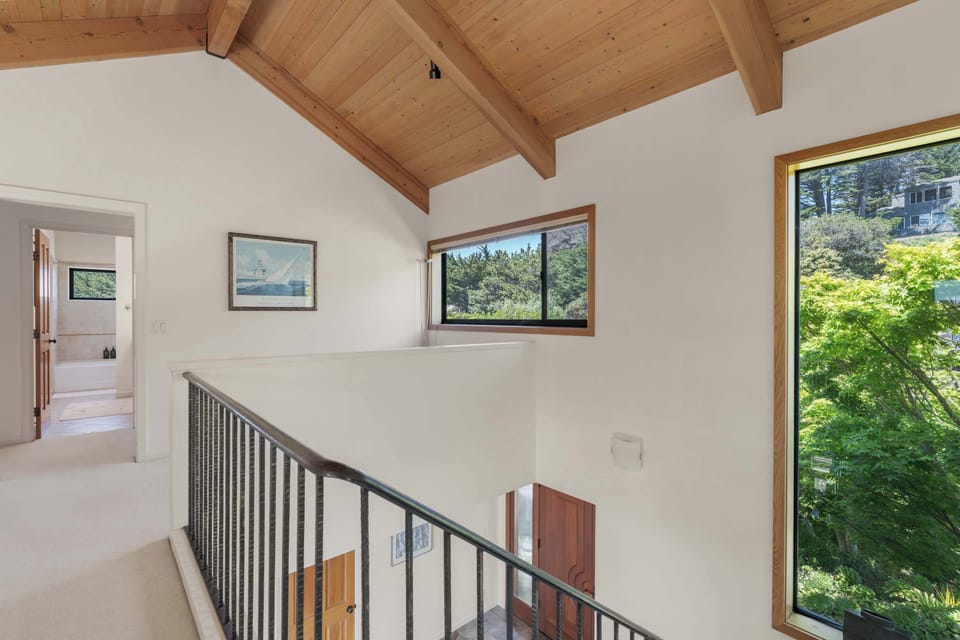 Landing at the top of the stairs lets the home breathe — art on the walls, a window deep into the cypress canopy, the great room visible below.