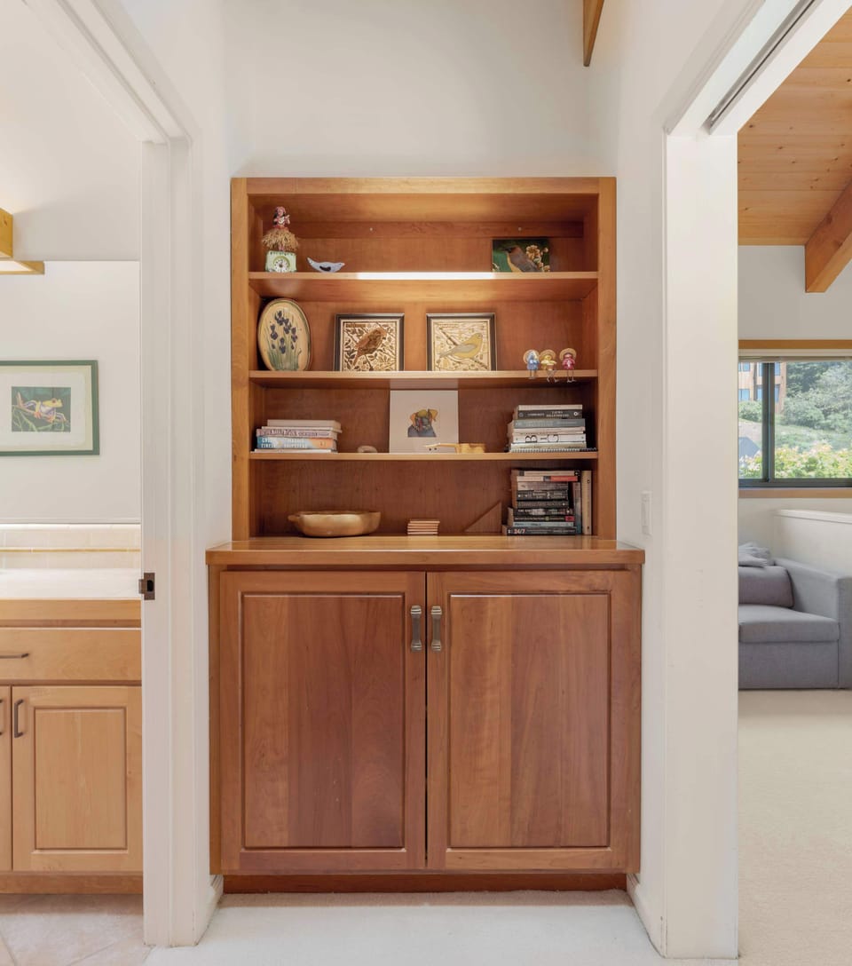 Built-in cherry shelving stocked with games, novels, and a small art collection — grab a paperback for the deck or a board game for the dining table.