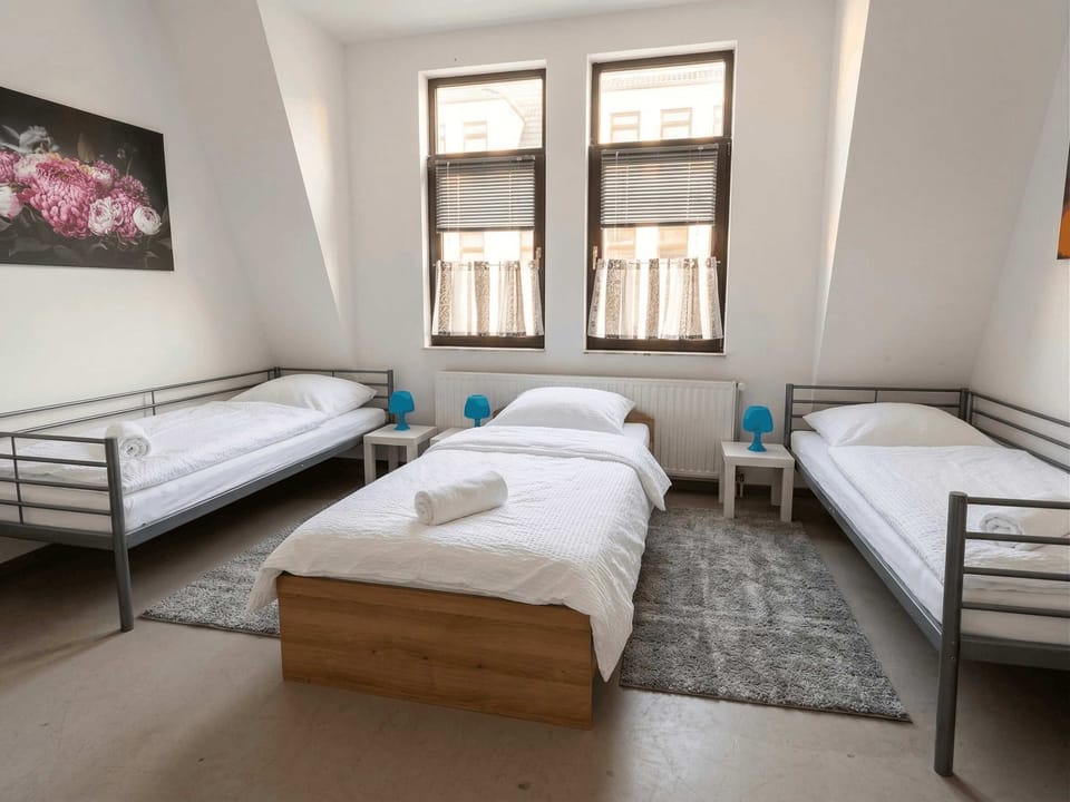 Schlafzimmer 1 (View 1) – Geräumiges Zimmer mit 3 Einzelbetten, Teppich, blauen Lampen, zwei Fenstern.