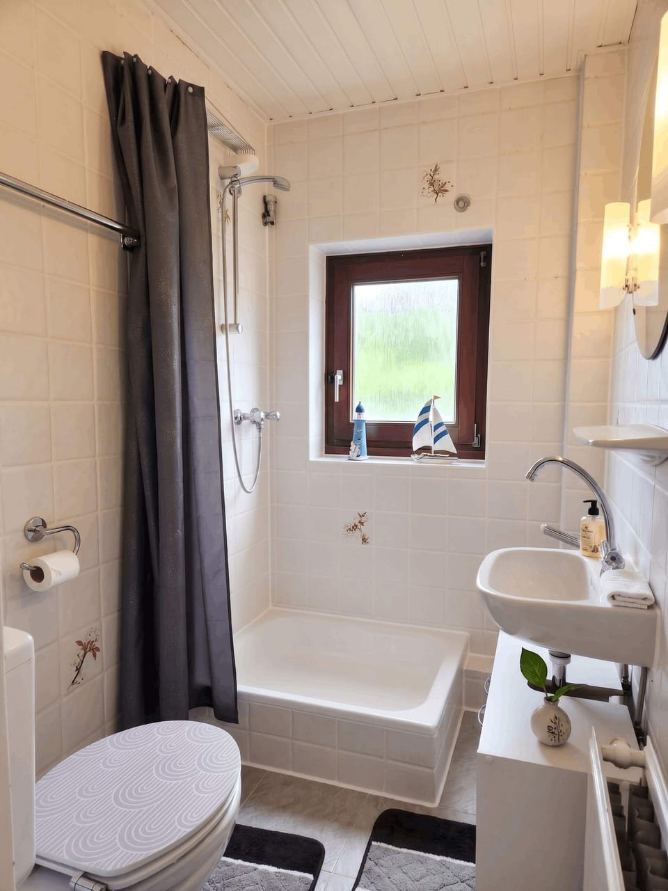 Bad – Helles Badezimmer mit Badewanne, Dusche, WC und Waschbecken. Maritimes Dekor, Holzdecke, Fenster.