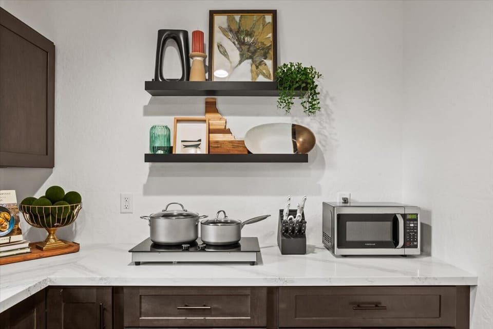 Kitchen cooktop station with dual burner induction, full knife block, microwave, and styled floating shelves — clean, curated, and guest-ready