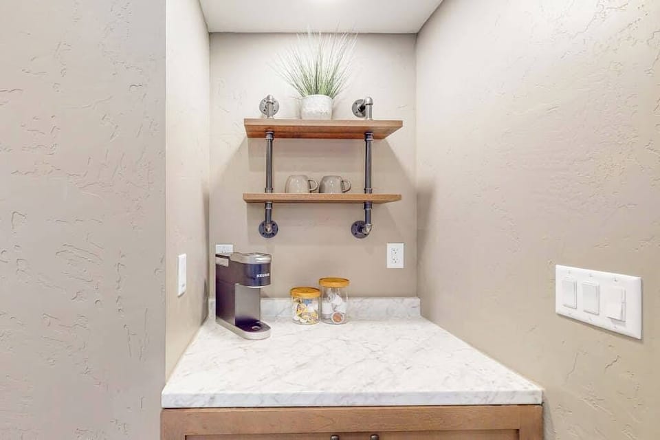 Dedicated coffee nook with Keurig, pipe shelves, and stocked mugs — morning sorted before you've unpacked
