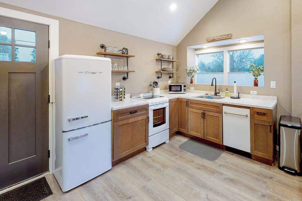 Bright full kitchen with retro white fridge, wood shaker cabinets, and open pipe shelving — everything you need to skip eating out