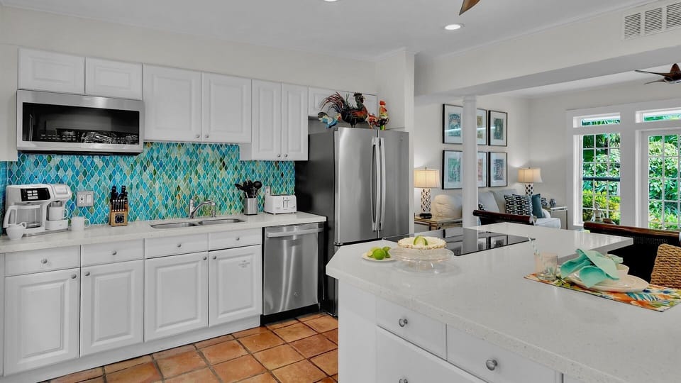 Picture yourself preparing fresh tropical meals in this bright kitchen with custom blue mosaic tile, modern appliances, and a spacious island perfect for gathering with loved ones.