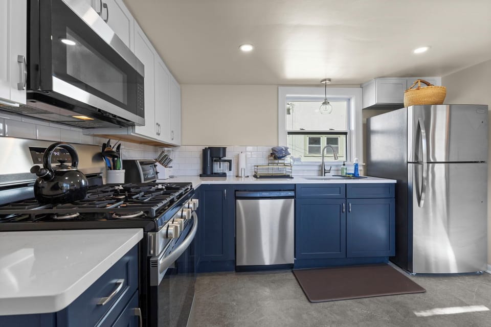 Full kitchen view featuring navy lower cabinets, white uppers, quartz countertops, stainless refrigerator, and dishwasher — stylish and fully stocked.