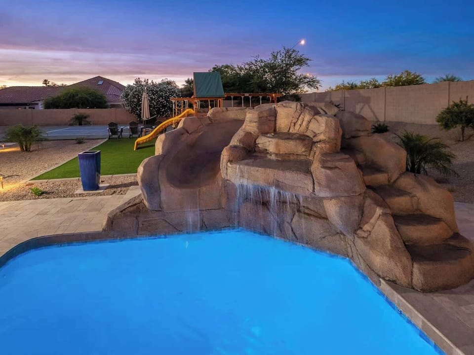 A stunning desert-themed pool featuring a rock waterfall and water slide surrounded by lush landscaping creates the perfect Arizona backyard paradise.