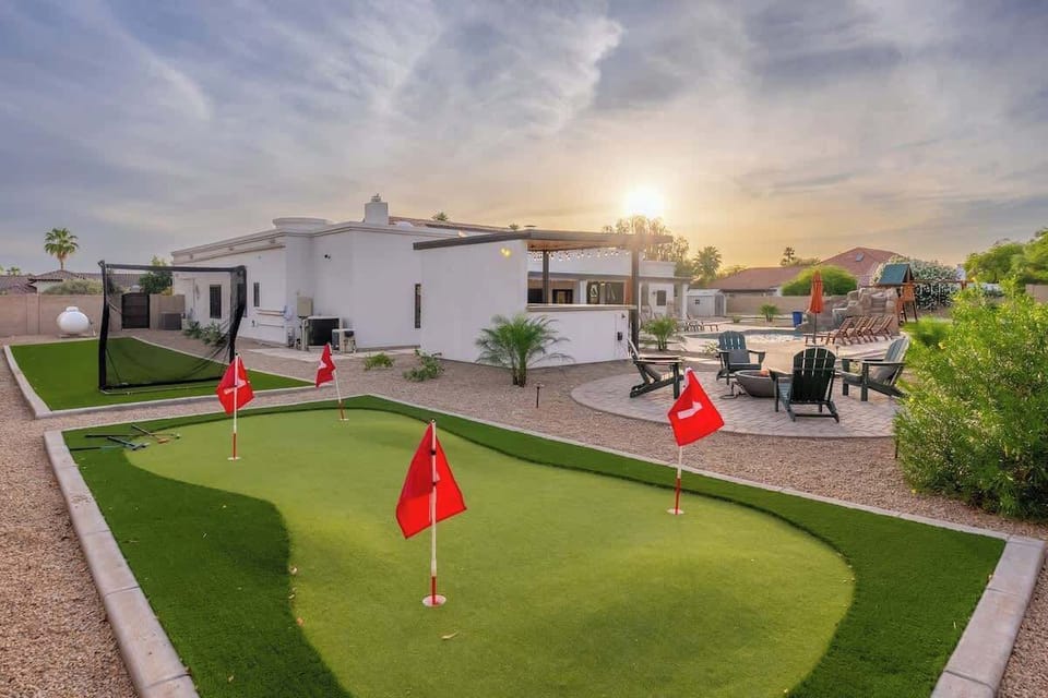 The property features a private putting green and sports court, surrounded by desert landscaping and multiple seating areas under a dramatic desert sunset.