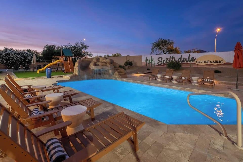 Large custom pool with waterslide and grotto invites endless fun, framed by plenty of loungers and a vibrant Scottsdale backdrop at dusk.